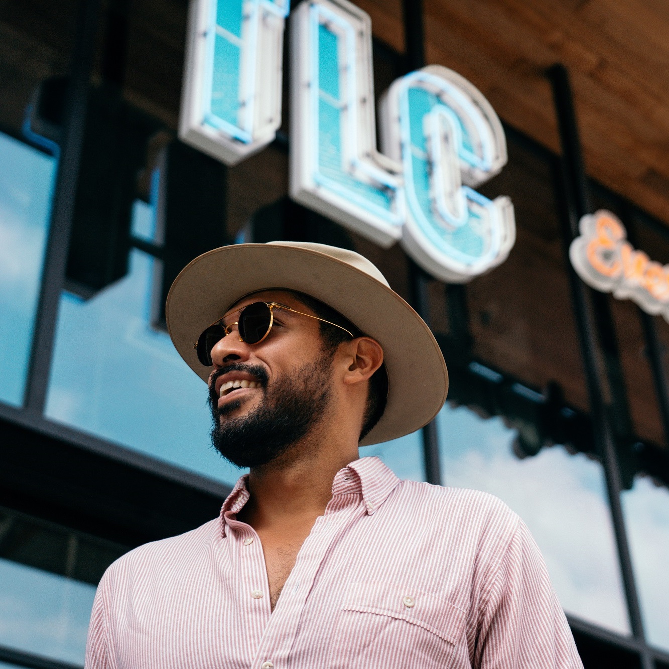 Man in hat and sunglasses smiling and walking by store